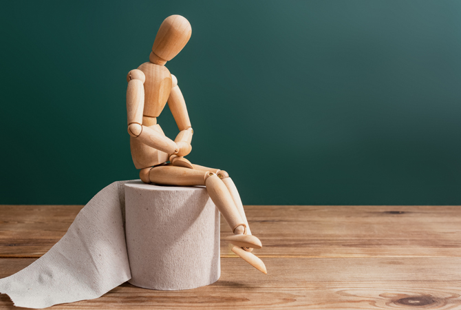 Wooden figure sit on a roll of toilet paper. Concept of the problem with digestion.